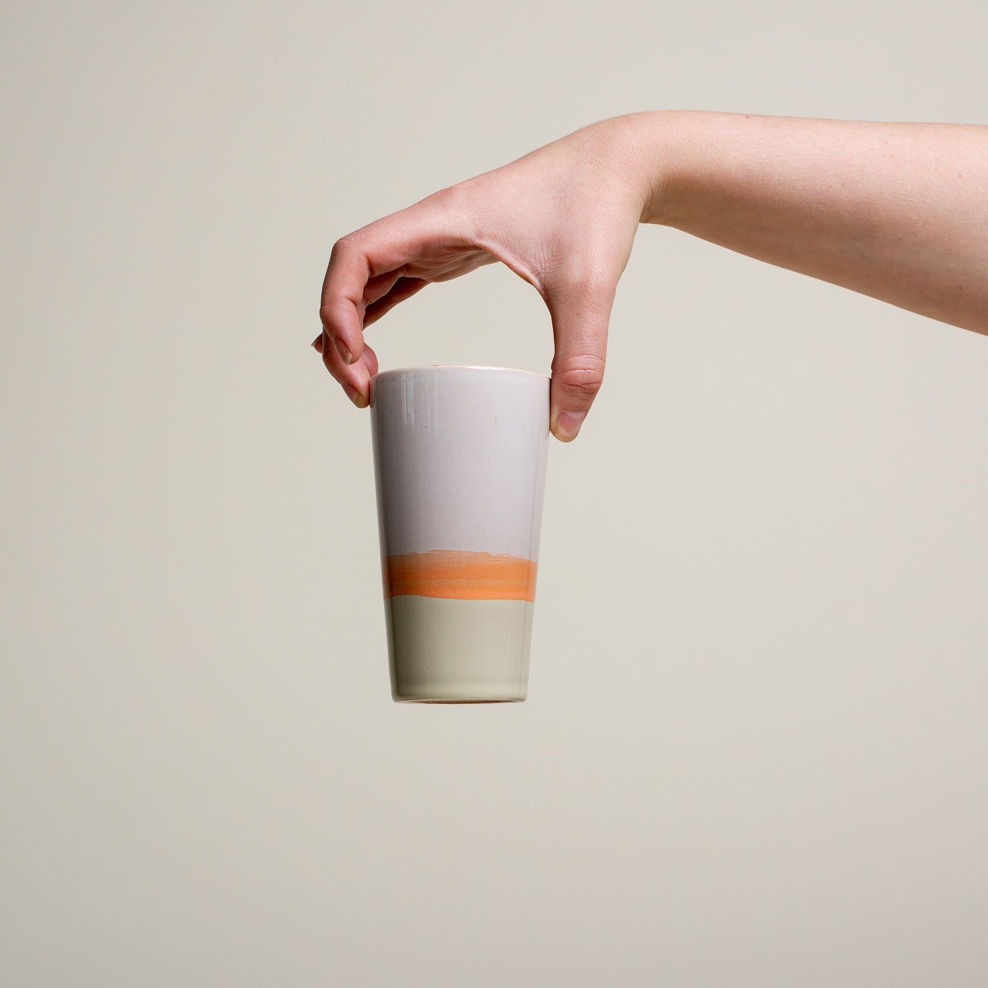 Eine Person hält eine Tasse in die Luft. Die Tasse im 70er retro Stil ist unten hell grün, in der mitte orange und oben hell grau gefärbt.