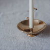 Nahaufnahme einer weißen Meditationskerze, stehend auf einer glänzenden Messingschale. In der Kerze stecken zwei Messingstifte. Ein Messingstift liegt in der Schale.