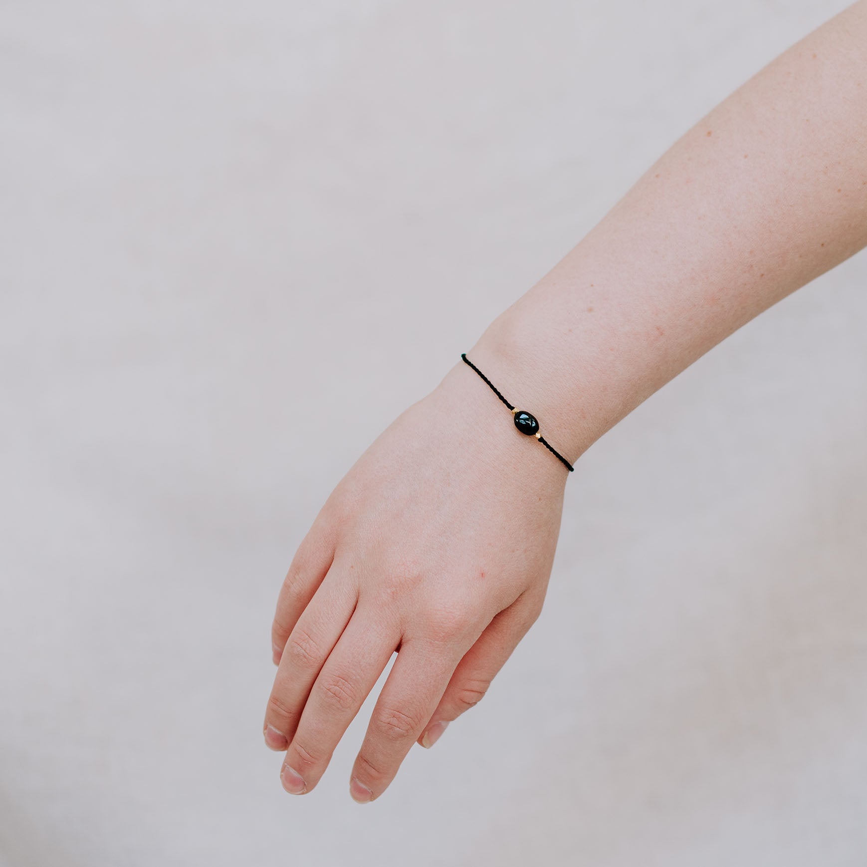 Eine Person trägt das A Beautiful Story Armband mit einem schwarzen Onyx Edelstein und Gold Details. Das Edelsteinarmband ist mit einem schwarzen Baumwollfade gefertigt. Der Edelstein steht für Fokus und Selbstbewusstsein.