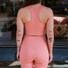 Primrose Compressive High Rise Leggings von Girlfriend Collective. Eine Person trägt eine Sport set in der Farbe Rosa. Die Leggins hat einen hohen Bund und ist nachhaltig produziert. Bild von der Hinterseite des Sets.